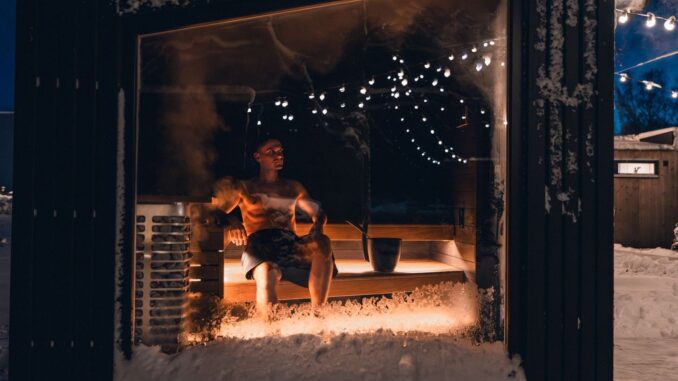 Person sitter i en varm bastu omgiven av snö och vintermörker