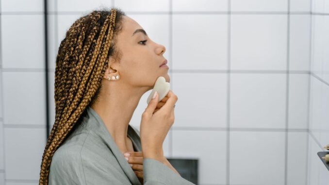 Kvinna använder en gua sha-sten längs käklinjen och halsen